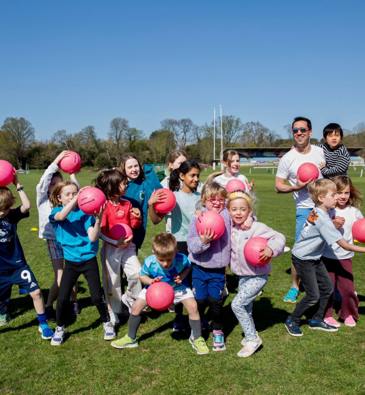 Five children posing together, smiling, on a grassy field.
