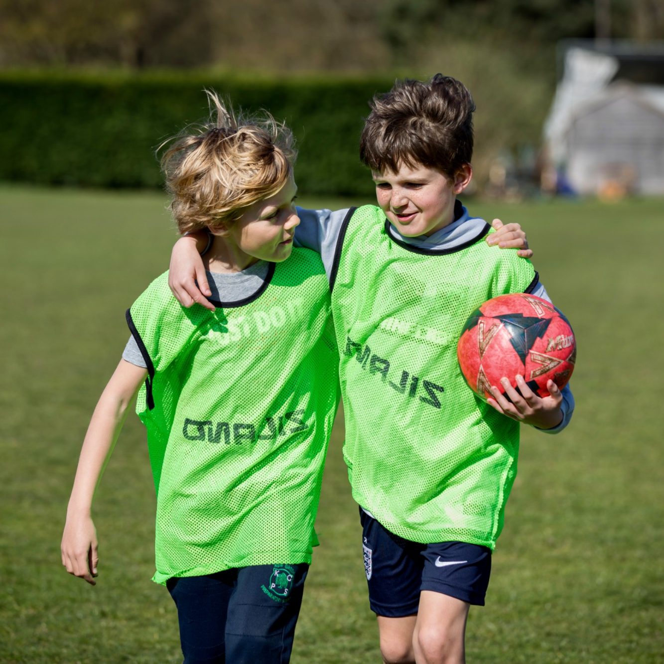 Four children hold pink balls, smiling in a grassy field on a sunny day.
